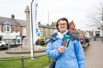 Woman stood in front of a Healthwatch flag holding up a leaflet about volunteering