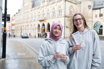 Two young teenagers holding up Healthwatch promotional material